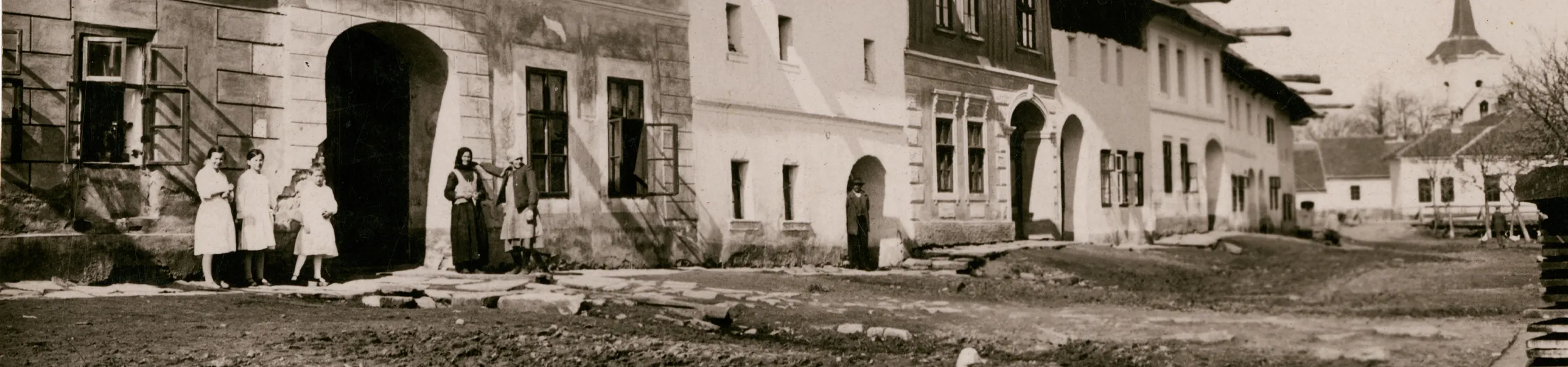 Čiernobiela fotografia oredvojnovej obce Tvarožná. Domy sa nachádzajú v ľavej časti fotky, na ceste vidieť husy. V pozadí je kostol. Fotku zhotovil prof. Alfréd Grosz (1885 - 1973) niekedy v druhej štvrtine 20. storočia.